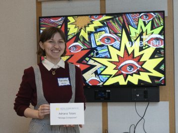 Adriana Totaro stands in front of a large monitor displaying their project.